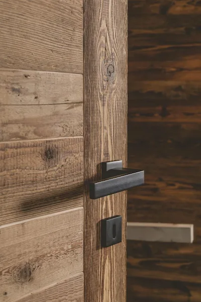 Porta | Dettaglio della maniglia in metallo nero su anta in legno antico Bardage marrone/beige