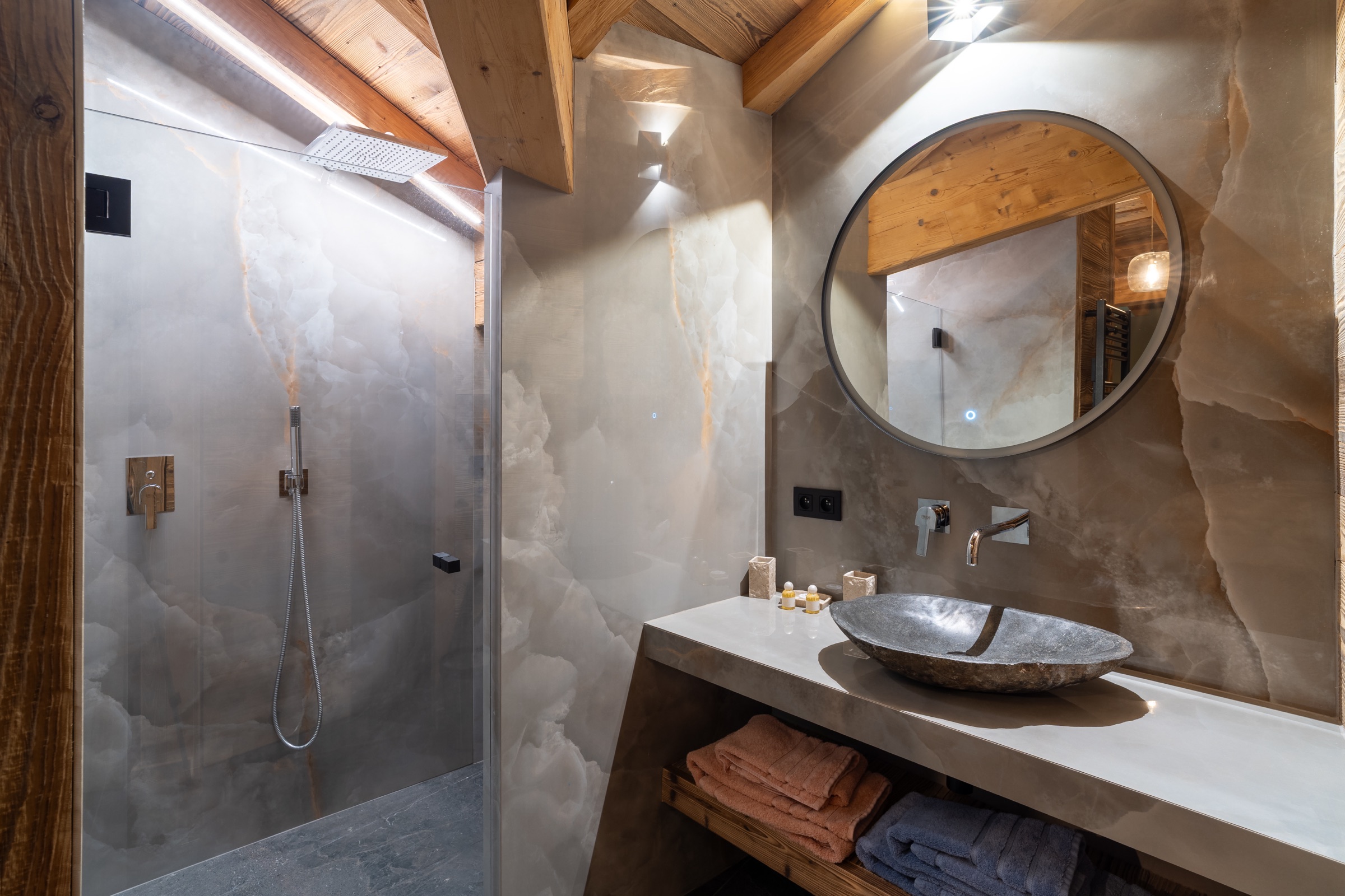 Salle de bains de chalet : parois en grès cérame grand format effet onyx, poutres en vieux bois, vasque en pierre